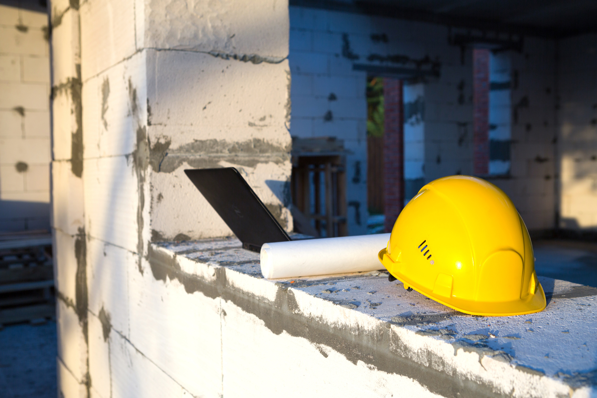 Construction hardhat, drawing and laptop on the window of a house under construction. Workflow, architecture and engineering. Tilbygning